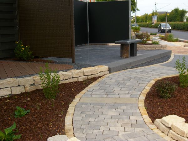 Gepflasterter Gartenweg mit Steinmauer und Bänken.