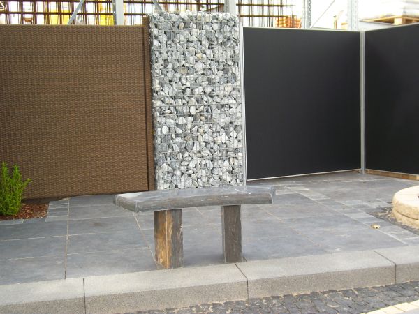 Steinbank vor Gabionenwand und Zaun.