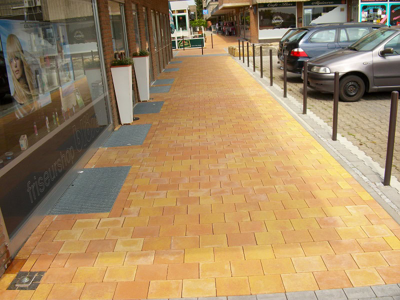 Gepflasterter Weg mit Geschäften und Autos.