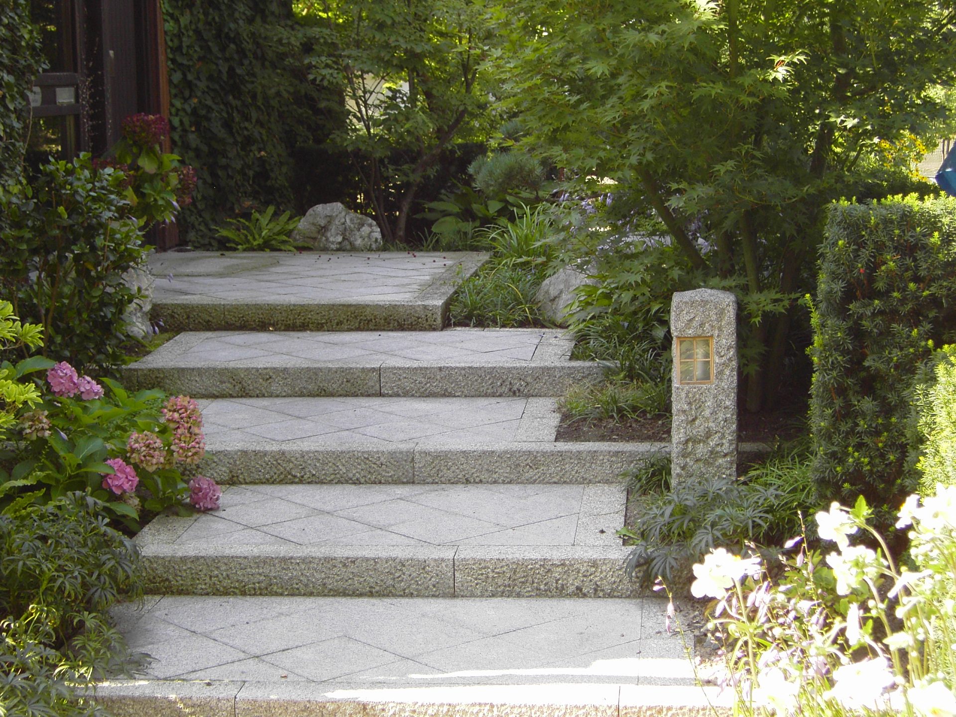 Steingarten-Treppe im Grünen, mit Blumen umrandet.