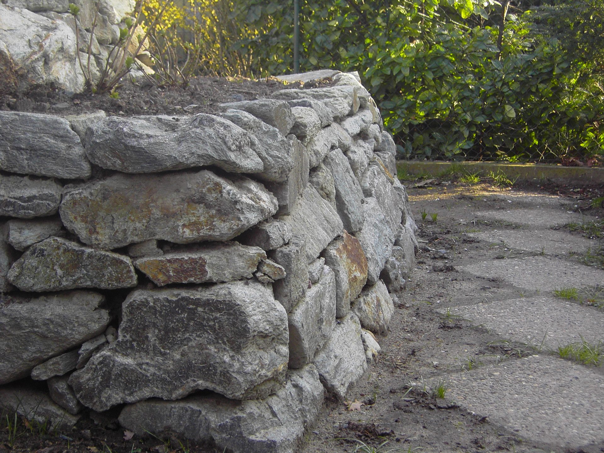 Steingartenmauer neben Gehweg im Grünen.