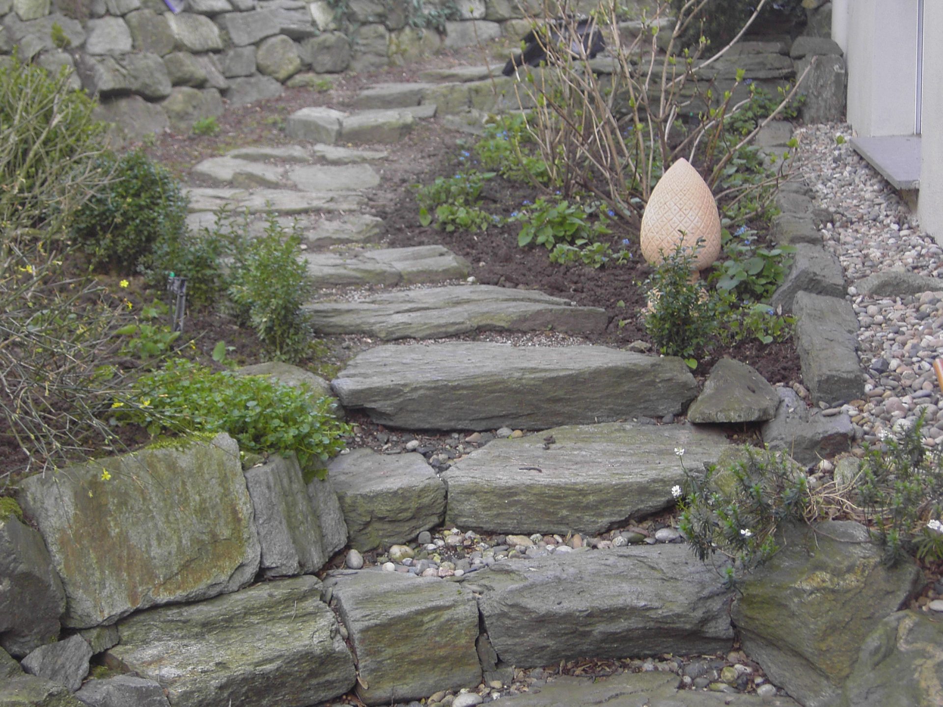 Steinweg mit Pflanzen und Dekor im Garten.