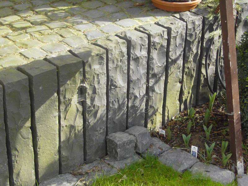 Steinmauer mit Pflanzen und Pflastersteinen im Garten