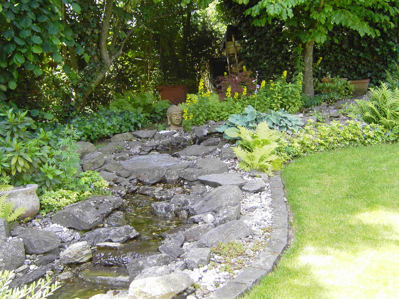 Steingarten mit fließendem Bach und Buddha-Statue.